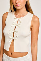 Young woman wearing a cream-colored sleeveless crop top with bow tie details on the front