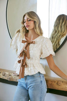 Women's textured blouse with satin bow accents, puff sleeves, and peplum hem – romantic and feminine top for casual and evening wear, perfect with jeans or skirts"