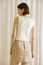 Model wearing a beige faux suede mini skirt with oversized front pockets, paired with a sleeveless cream knit top. The skirt is styled in a minimalist, neutral-tone setting, ideal for a chic fall outfit.