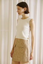 Model wearing a beige faux suede mini skirt with oversized front pockets, paired with a sleeveless cream knit top. The skirt is styled in a minimalist, neutral-tone setting, ideal for a chic fall outfit.