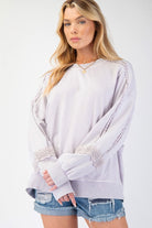 A relaxed-fit terry knit pullover with a mineral-washed finish, featuring crochet lace detailing on the sleeves, a crew neckline, and dropped shoulders. Styled with ribbed cuffs and a raw hem for a chic, casual look.