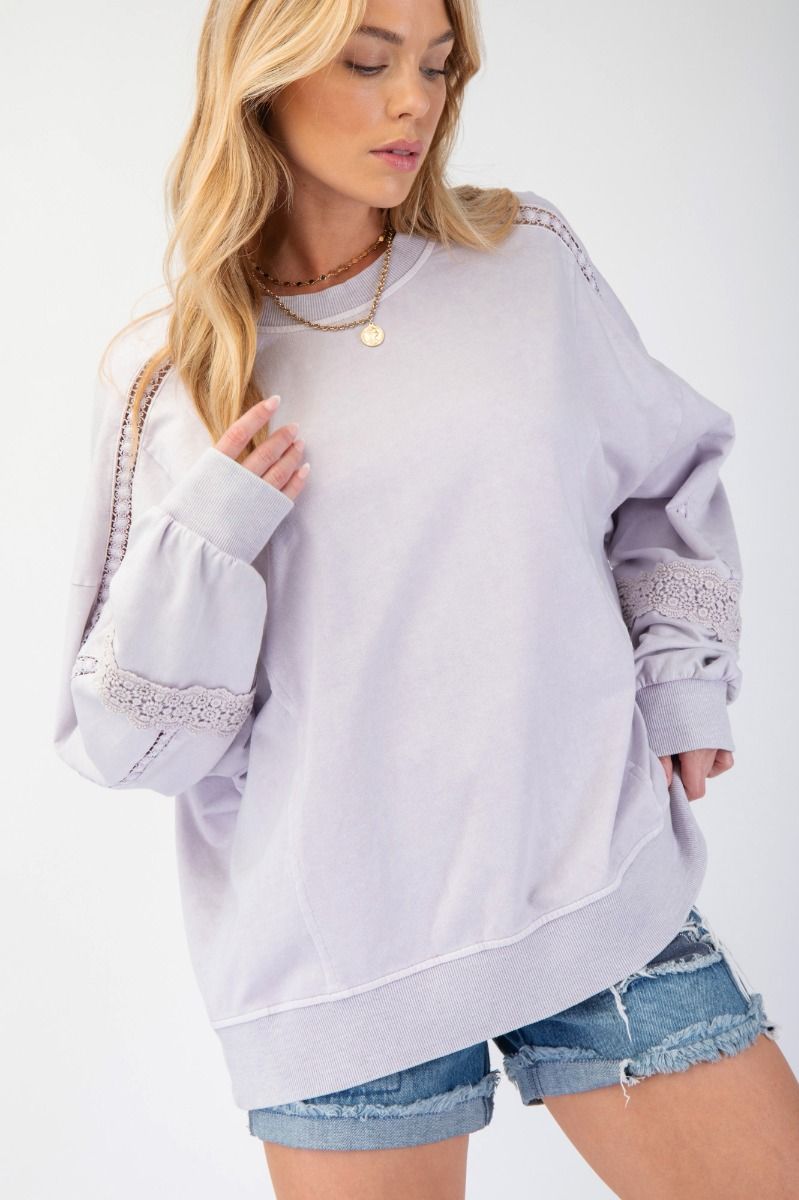 A relaxed-fit terry knit pullover with a mineral-washed finish, featuring crochet lace detailing on the sleeves, a crew neckline, and dropped shoulders. Styled with ribbed cuffs and a raw hem for a chic, casual look.