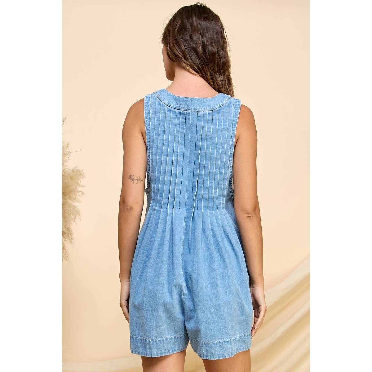 Model wearing a sleeveless denim-style romper in charcoal with a front tie detail, pleated front, and side pockets, perfect for casual outings and everyday style.