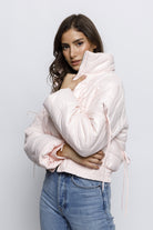 Woman wearing a light pink puffer jacket with bow details on the front and sleeves. The jacket has a high collar and quilted design, giving it a cozy and stylish look.