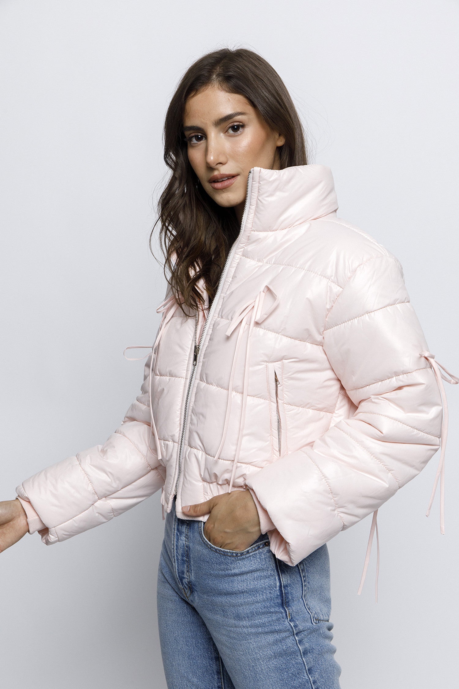  Woman wearing a light pink puffer jacket with bow details on the front and sleeves. The jacket has a high collar and quilted design, giving it a cozy and stylish look.