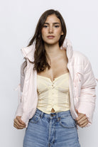 Woman wearing a light pink puffer jacket with bow details on the front and sleeves. The jacket has a high collar and quilted design, giving it a cozy and stylish look. 