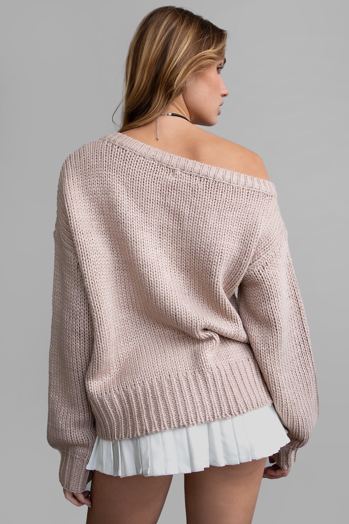 Model wearing an oversized, off-the-shoulder ribbed knit sweater in a soft neutral color, paired with a white pleated mini skirt for a cozy, casual look