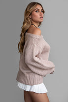 Model wearing an oversized, off-the-shoulder ribbed knit sweater in a soft neutral color, paired with a white pleated mini skirt for a cozy, casual look