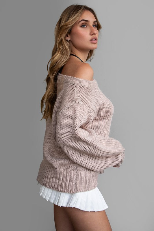 Model wearing an oversized, off-the-shoulder ribbed knit sweater in a soft neutral color, paired with a white pleated mini skirt for a cozy, casual look