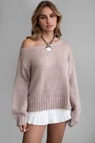 Model wearing an oversized, off-the-shoulder ribbed knit sweater in a soft neutral color, paired with a white pleated mini skirt for a cozy, casual look